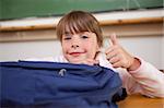 Cute schoolgirl posing with a bag and the thumb up in a classroom