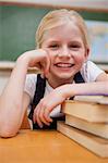 Portrait of a smiling girl leaning on books in a classroom