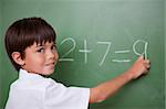 Happy schoolboy writing an addition on a chalkboard