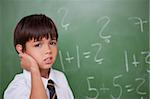 Confused schoolboy thinking while scratching the back of his head in a classroom