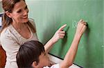 Schoolteacher helping a schoolboy doing an addition on a blackboard