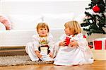 Two cute twins girl sitting with presents boxes near Christmas tree