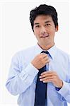 Portrait of a smiling businessman fixing his tie against a white background