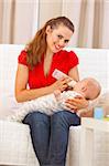 Happy mother sitting on couch and feeding baby