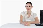 Businesswoman drinking a takeaway coffee while using a computer against a white background