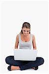 Cross-legged woman using a laptop against a white background