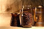 Glass jar with coffee beans near old copper coffeepot on canvas background
