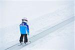 Junior skier. Little cute boy in a ski outfit rises on lift on hill