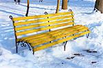 Yellow wooden bench among the snowbanks in winter park on a sunny fine day