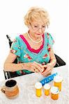 Disabled senior woman in a wheelchair, counting out her medications for the week.  White background.