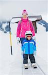 In ski school. Little cute boy in ski goggles and a helmet with his mother on the skier lift