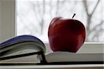 An apple lay on book next to window