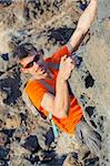 Young man in glasses with backpack climbing indoor wall. Vertical view