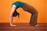Young woman performs upward bow posture over orange background