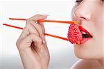 The sexy girl holds chopsticks a raspberry near lips