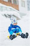 Cute little boy in blue riding on a sled near  the Austrian cottage