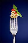 delicious italian pasta with tomato sauce and basil on fork over blue background