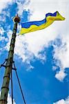 Flag of Ukraine with flag pole waving in the wind on front of blue sky with clouds