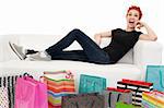 An crazy happy shopping girl sitting on a white couch surrounded with shopping bags.