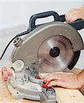 Worker hands cutting wooden plank with electric circular saw - closeup