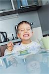 Happy little cute boy in pajamas eating breakfast at a table in the kitchen. Vertical view