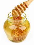 Honey in a transparent jar showing a piece of honey comb wax and a wooden stick on white background