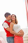 Portrait of pregnant woman with husband hugging her tummy