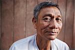 Portrait of happy mature asian man looking at camera against brown wall. Copy space