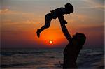Mother and little son silhouettes on beach at sunset