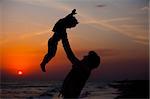 Father and little son silhouettes on beach at sunset