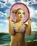 fashion shot of blond sensual girl in bikini andtaking pose with hat on and hair style