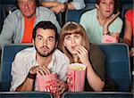 Scared Caucasian couple eating popcorn in theater