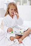 Little girl with a bad case of influenza using nasal spray and a box of paper tissues
