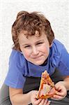 Boy with a slice of pizza sitting on the floor