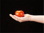 Childs hand with tomatoe and palm facing up - on black background