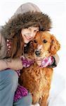 smiling teenager caucasian girl in hood hugging her dog outdoors at snow