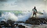 Surfer Standing on Rocks with Rough Seas