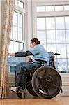 Homme avec une lésion médullaire en regardant par la fenêtre de sa maison accessible fauteuil roulant