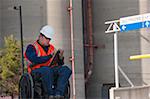 Facilities engineer in a wheelchair inspecting outdoor bulk storage tanks and recording data