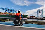 Transportation engineer in wheelchair inspecting container ship at shipping port