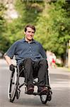 Man with spinal cord injury in a wheelchair maneuvering wheelchair on path through public park