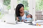 Mother holding baby son, with laptop and coffee cup