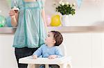 Baby boy in high chair and looking up and mother with birthday cupcake