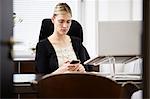 Businesswoman at desk, looking at cellphone