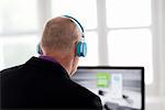 Businessman listening to headphones, using computer in office