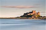 Bamburgh Castle bathed in golden evening light overlooking Bamburgh Bay with the sea filling the foreground, Northumberland, England, United Kingdom, Europe