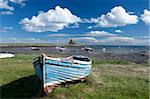 Old wooden fishing boat on a grassy bank with Lindisfarne harbour and Lindisfarne Castle in the background, Holy Island (Lindisfarne), Northumberland, England, United Kingdom, Europe