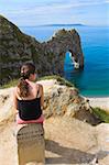 Woman resting on a clifftop sign, looking towards Durdle Door beach, Jurassic Coast, UNESCO World Heritage Site, Dorset, England, United Kingdom, Europe