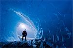 COMPOSITE : Vue depuis l'intérieur d'une grotte de glace d'iceberg congelé dans le lac Mendenhall comme un grimpeur de glace se trouve à l'entrée, Juneau, sud-est de l'Alaska, hiver