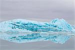 Blue iceberg from Sheridan Glacier reflects on thin film of water over ice, Chugach Mountains near Cordova, Southcentral Alaska, Winter